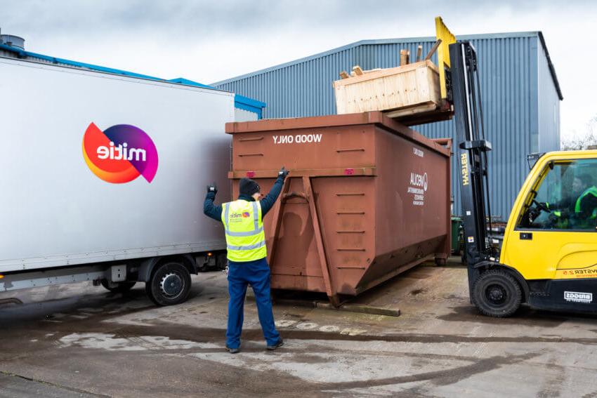 A man in a Mitie hi-vis vest directing wood to be disposed of in a large 'Wood Only' bin